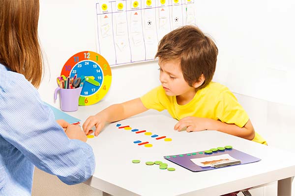 young boy in a yellow shirt working with a woman in a blue shirt on a puzzle